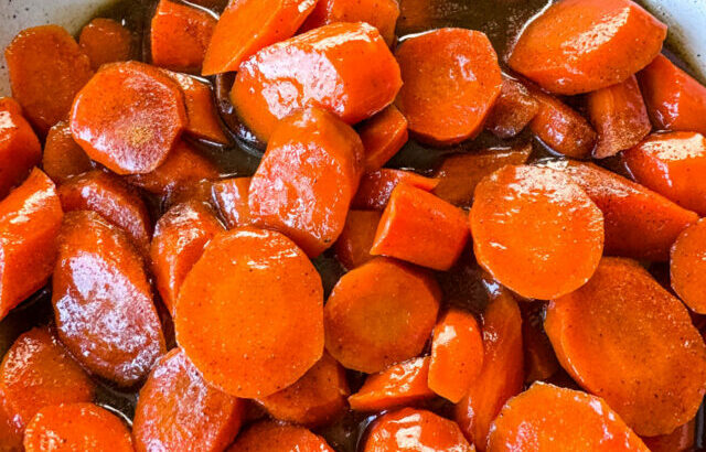 candied carrots with brown sugar cinnamon glaze in a white bowl with a wooden spoon