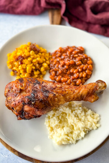 grilled turkey legs on a plate with baked beans, coleslaw, and fried corn