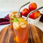 homemade peach tea in a glass with basil, peaches, and a straw