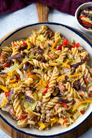 taco pasta salad with chips, cheese, and lettuce, in a white bowl