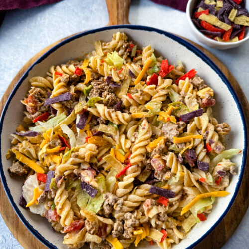 taco pasta salad with chips, cheese, and lettuce, in a white bowl