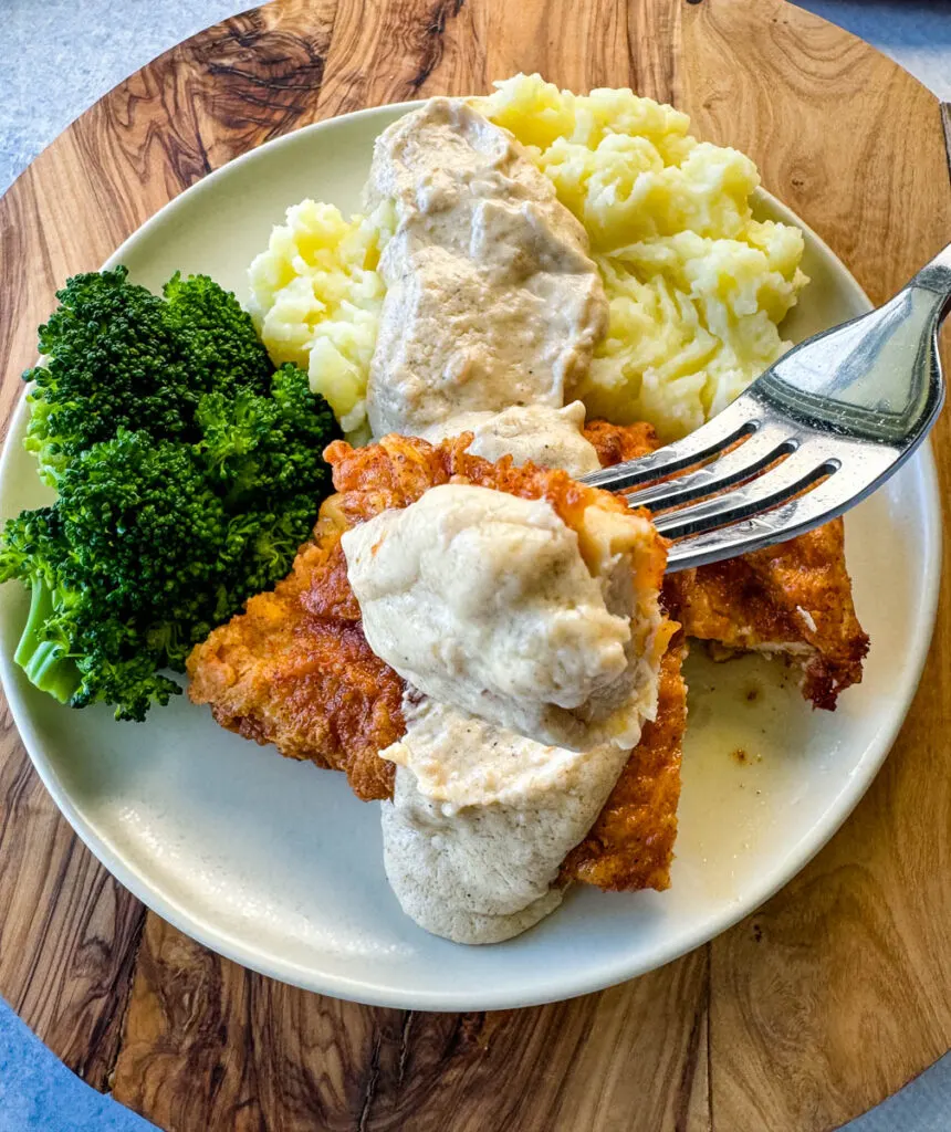 a piece of chicken fried chicken with gravy held by a fork