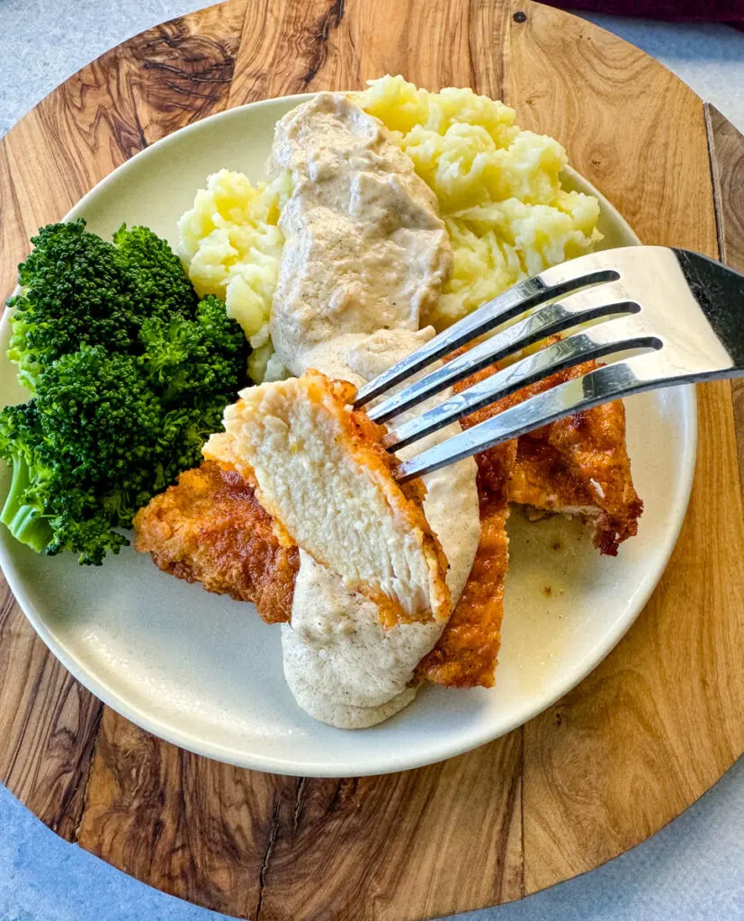 a piece of chicken fried chicken with gravy held by a fork