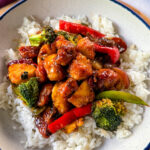 orange chicken with stir fry vegetables and white rice in a white bowl