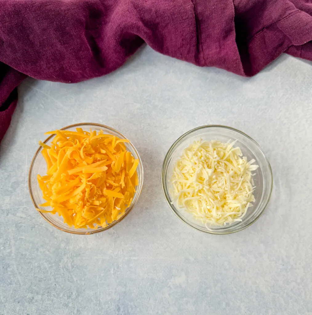 grated cheddar cheese and mozzarella cheese in separate glass bowls