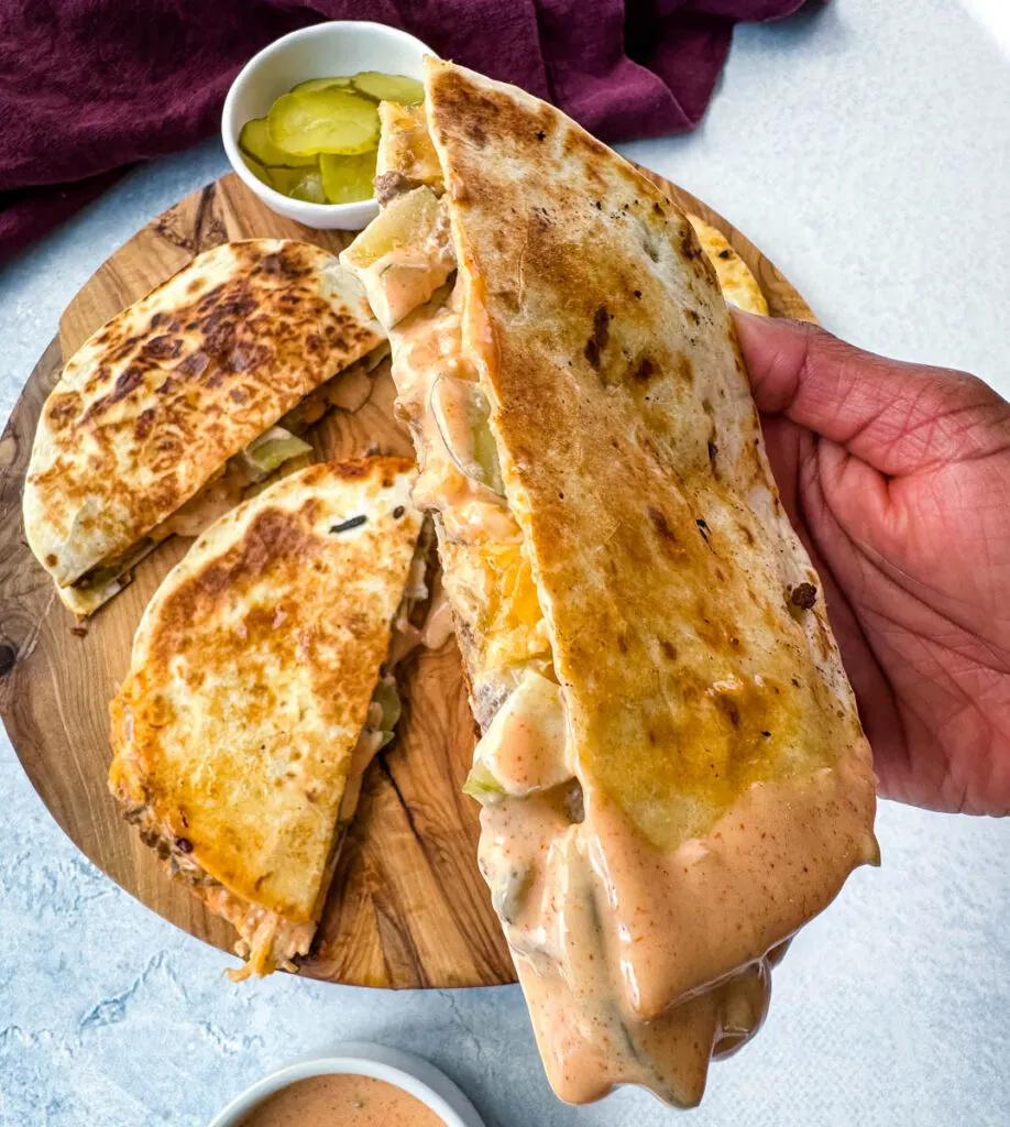 person holding cheeseburger quesadilla with pickles and burger sauce