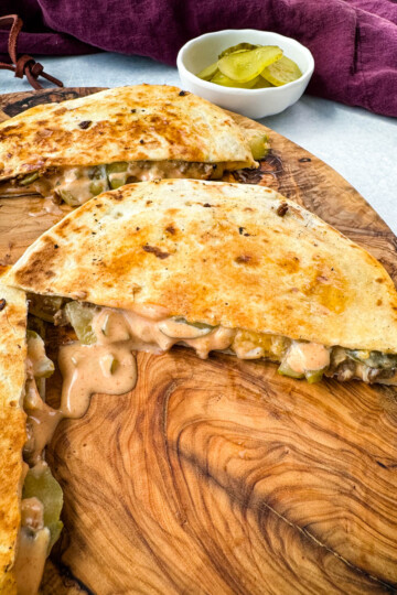 cheeseburger quesadilla with pickles and burger sauce on a wooden cutting board