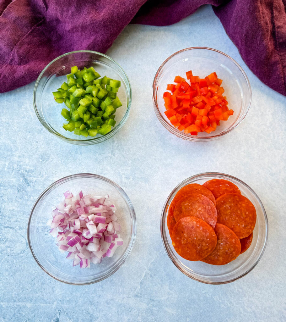 diced green peppers, diced red peppers, diced onions, and pepperoni in separate glass bowls