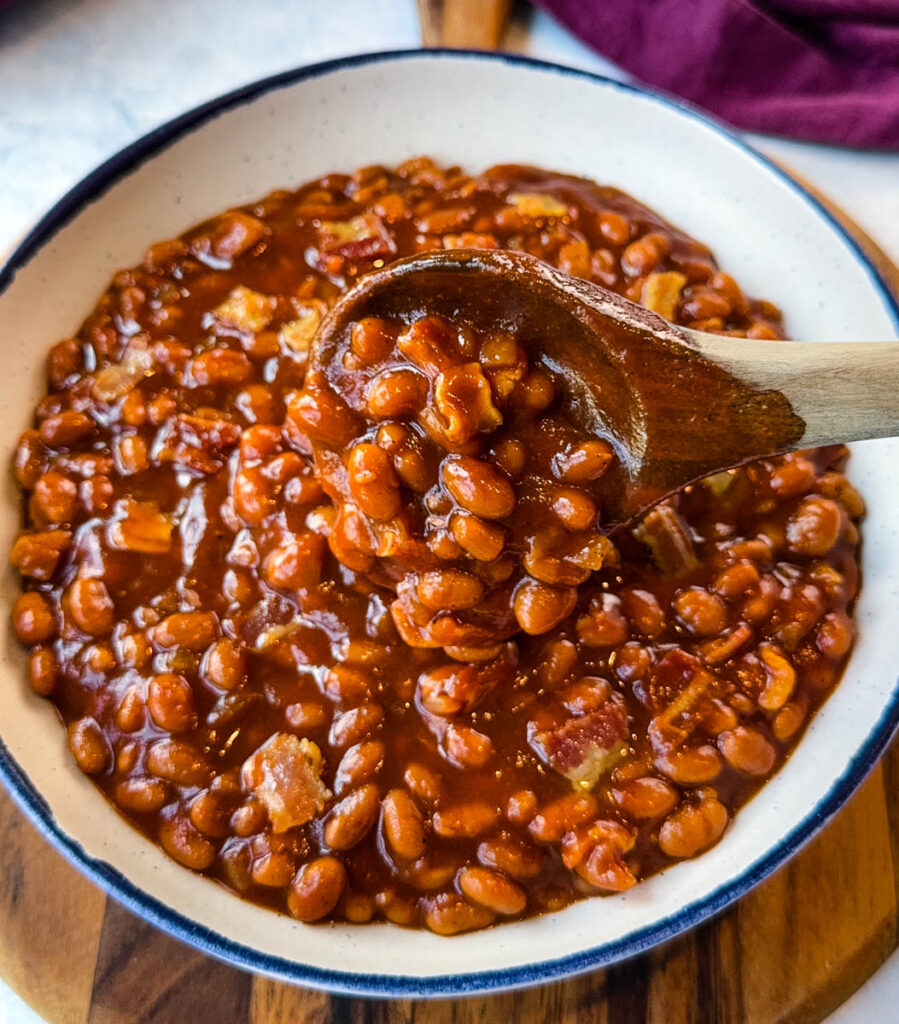 slow cooker Crockpot baked beans in a white bowl with a wooden spoon