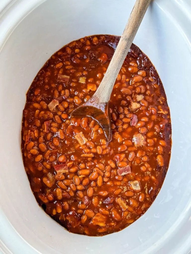 baked beans in a slow cooker Crockpot with a wooden spoon