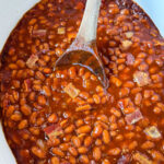 baked beans in a slow cooker Crockpot with a wooden spoon