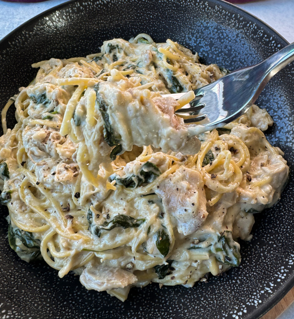 a forkful of slow cooker Crockpot chicken alfredo in a black bowl