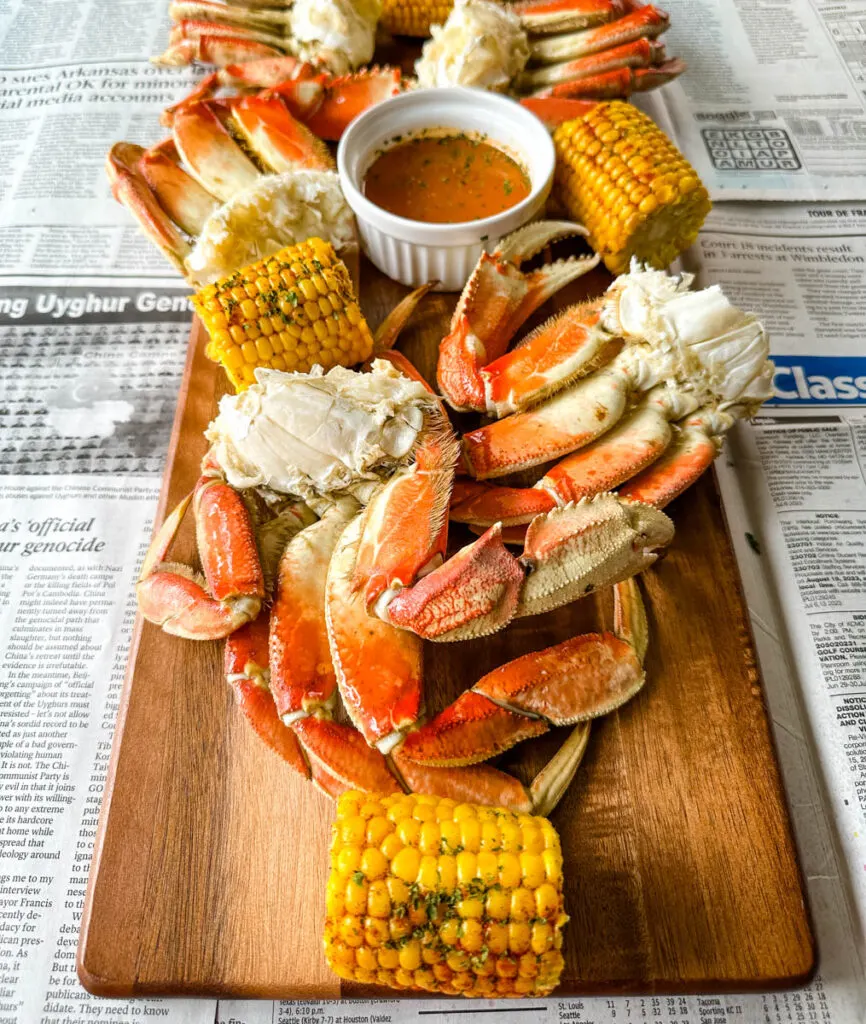 Dungeness crab legs on a platter with corn on the cob and lemon garlic butter sauce