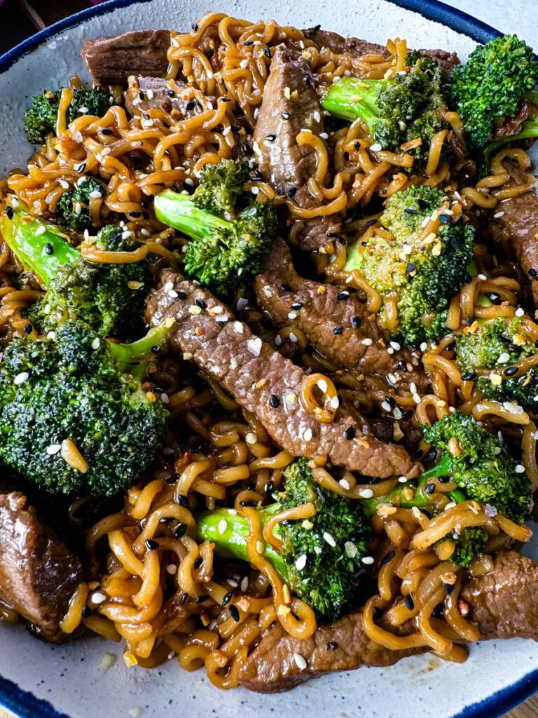 beef and broccoli stir fry with ramen noodles in a white bowl