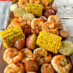 shrimp boil with andouille sausage, red potatoes, and corn on the cob on a flat surface with newspaper