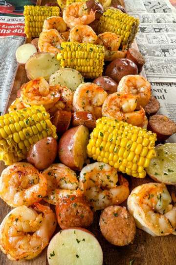 shrimp boil with andouille sausage, red potatoes, and corn on the cob on a flat surface with newspaper