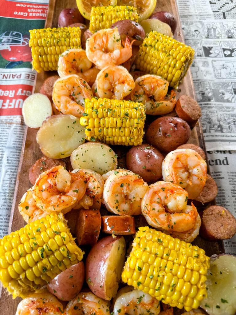 shrimp boil with andouille sausage, red potatoes, and corn on the cob on a flat surface with newspaper