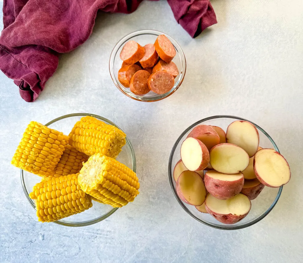 andouille sausage, corn on the cob, and red potatoes in separate glass bowls