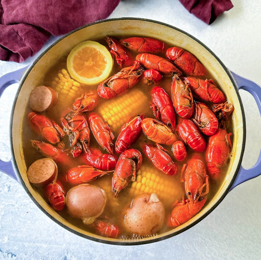 crawfish, corn on the cob, lemon, bay leaf, potatoes, and sausage in a large Dutch oven with crawfish boil sauce