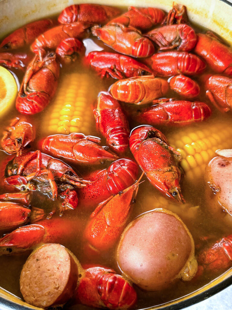 crawfish, corn on the cob, lemon, bay leaf, potatoes, and sausage in a large Dutch oven with crawfish boil sauce