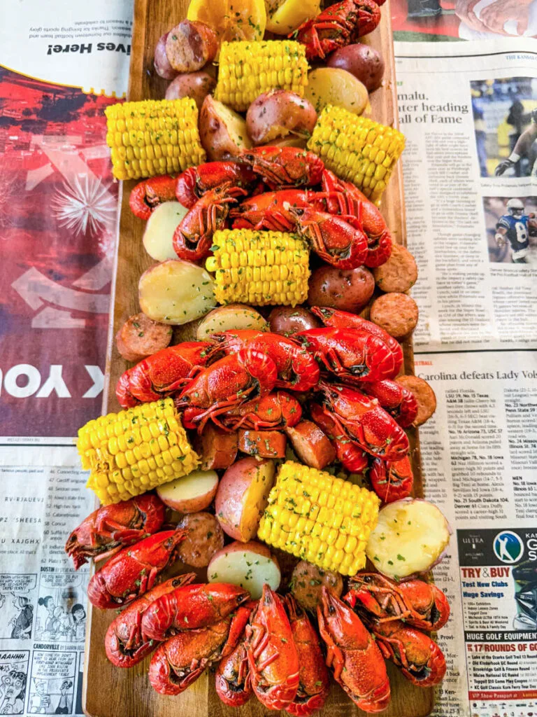 crawfish boil on a platter with corn, red potatoes, sausage, and butter with newspaper