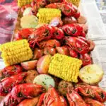 crawfish boil on a platter with corn, red potatoes, sausage, and butter with newspaper