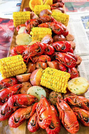 crawfish boil on a platter with corn, red potatoes, sausage, and butter with newspaper