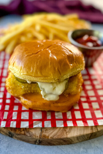 fish sandwich with cheese, pickles, and tartar sauce on a brioche bun on a plate with fries