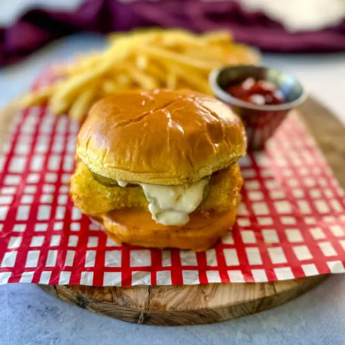 fish sandwich with cheese, pickles, and tartar sauce on a brioche bun on a plate with fries