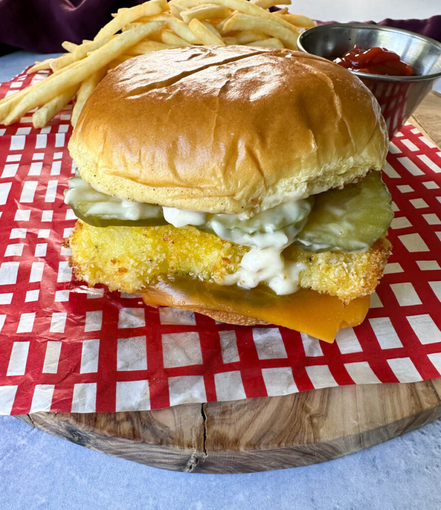 fish sandwich with cheese, pickles, and tartar sauce on a brioche bun on a plate with fries