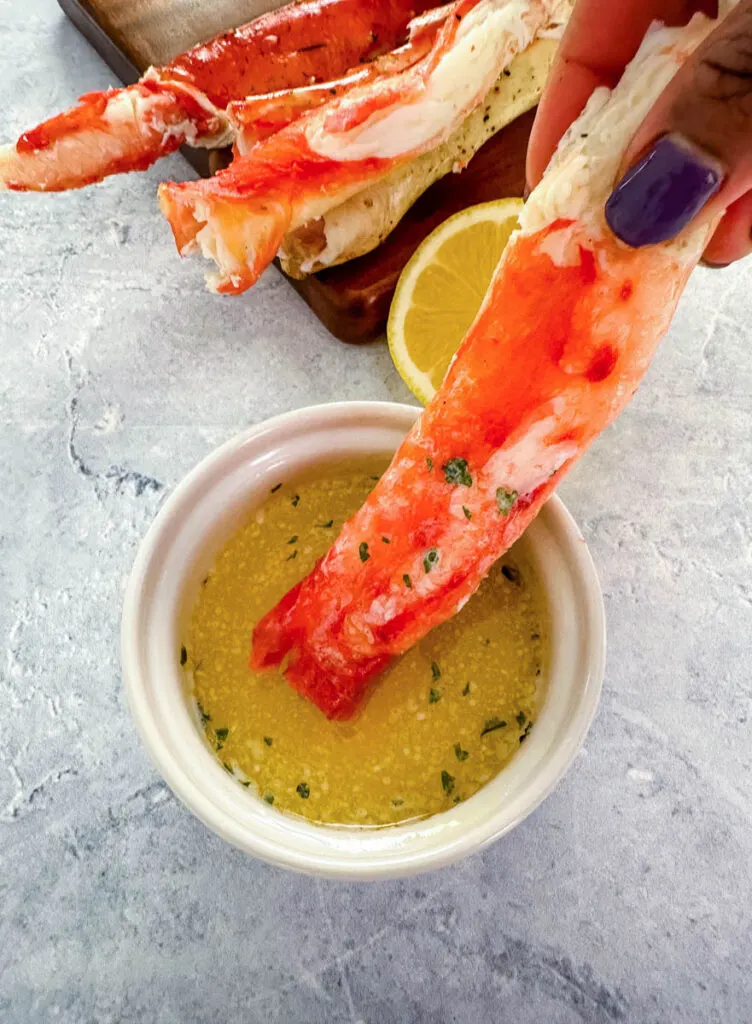 person holding cracked king crab leg in melted butter