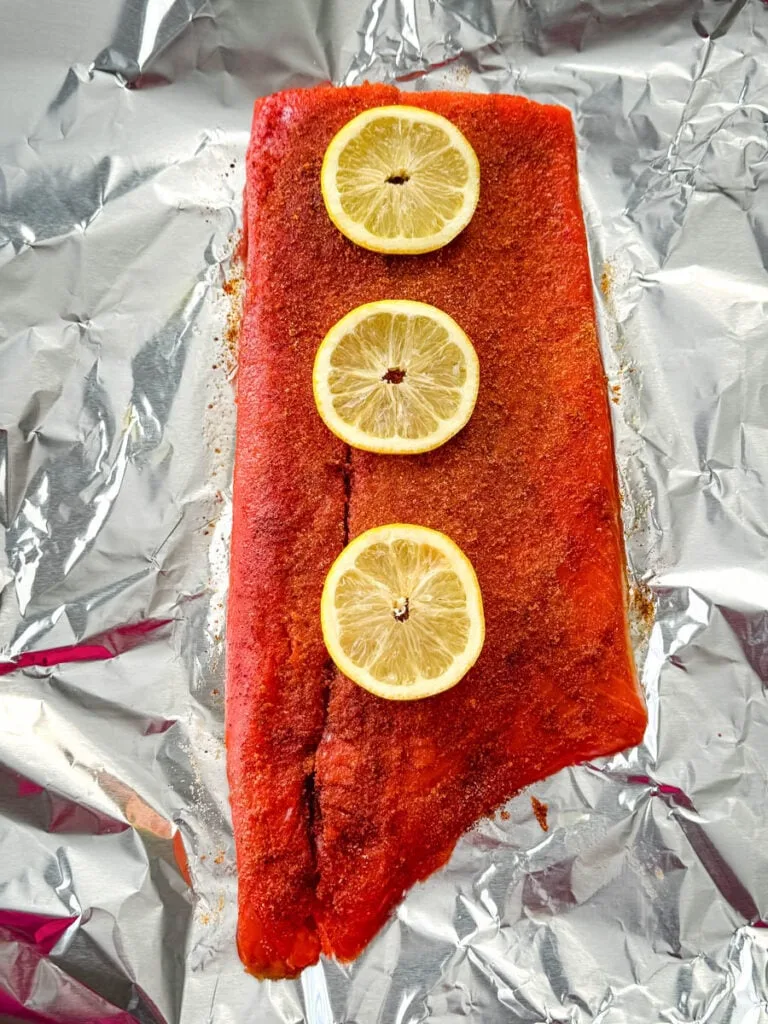 raw seasoned salmon on foil with fresh lemons