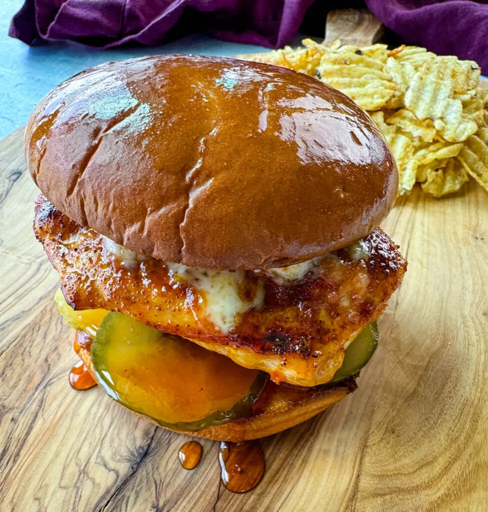hot honey chicken sandwich with a brioche bun, pickles, and pepperjack cheese on a plate with chips