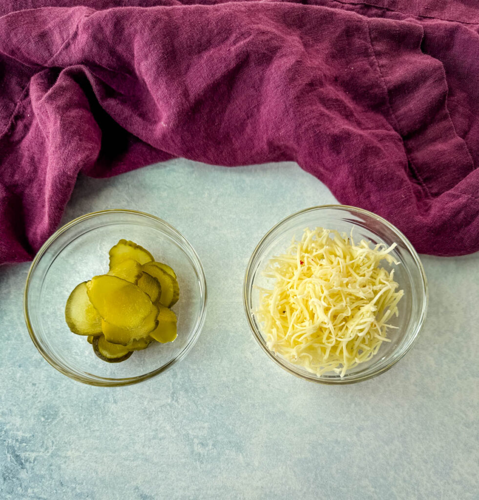 pickles and grated pepper jack cheese in separate glass bowls