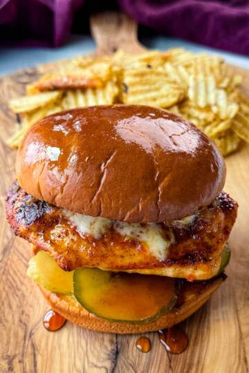 hot honey chicken sandwich with a brioche bun, pickles, and pepperjack cheese on a plate with chips