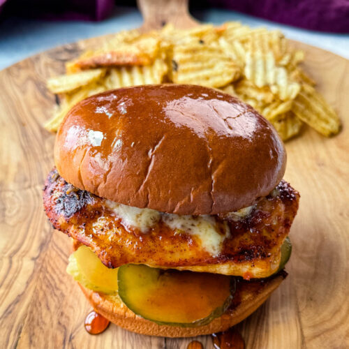 hot honey chicken sandwich with a brioche bun, pickles, and pepperjack cheese on a plate with chips