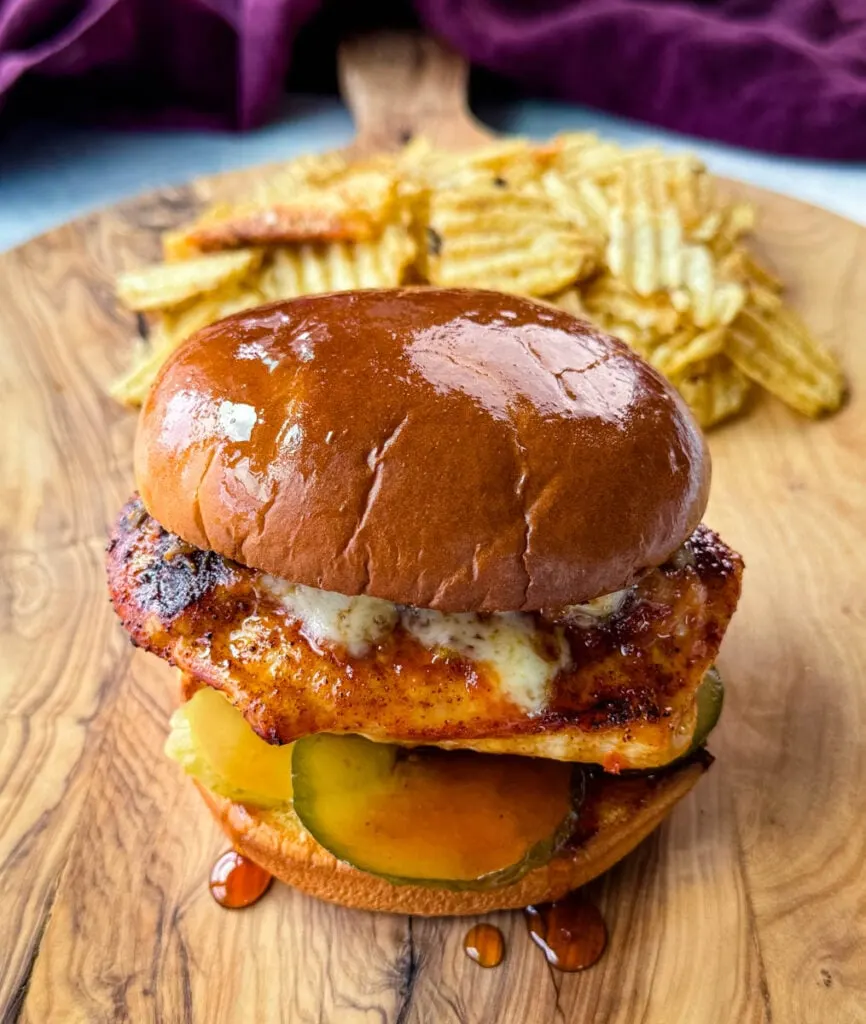 hot honey chicken sandwich with a brioche bun, pickles, and pepperjack cheese on a plate with chips