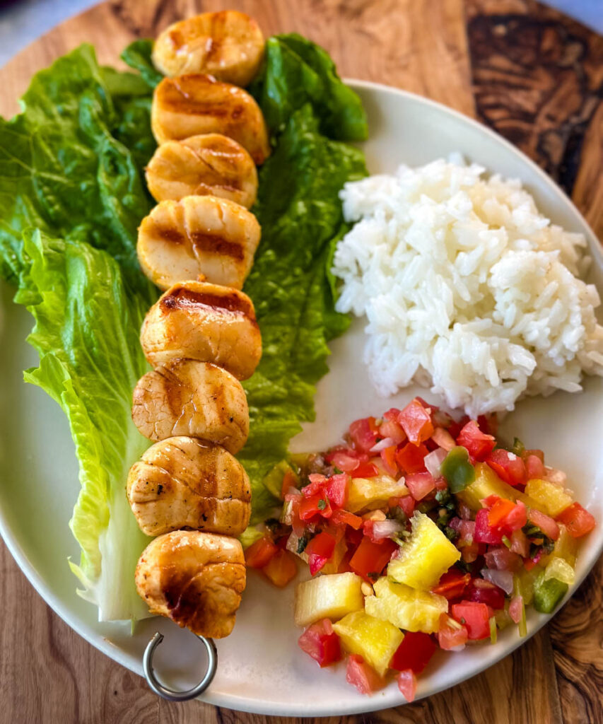 grilled scallops on a plate with lettuce, rice, and vegetables