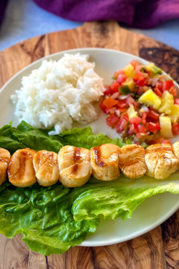 grilled scallops on a plate with lettuce, rice, and vegetables