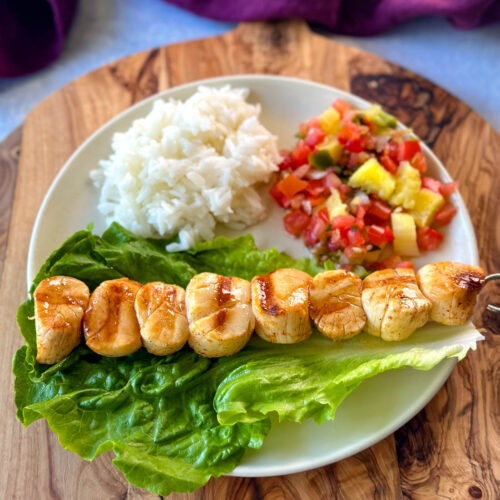 grilled scallops on a plate with lettuce, rice, and vegetables