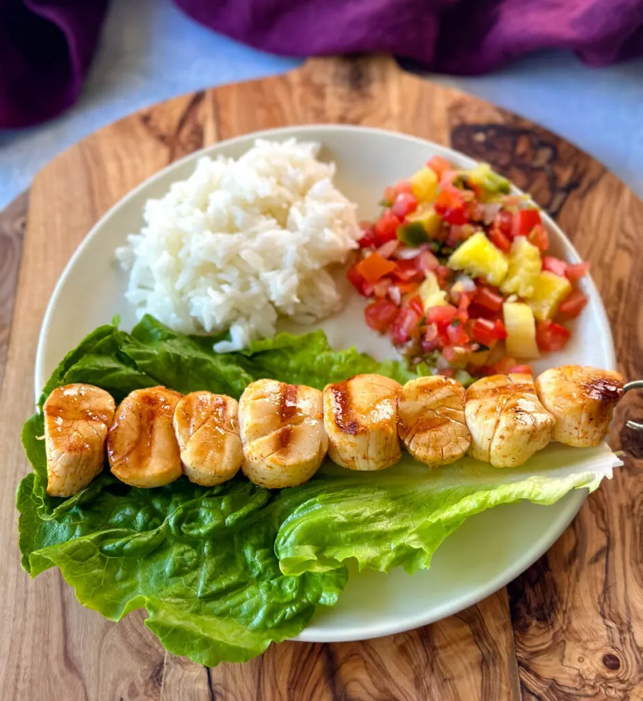 grilled scallops on a plate with lettuce, rice, and vegetables