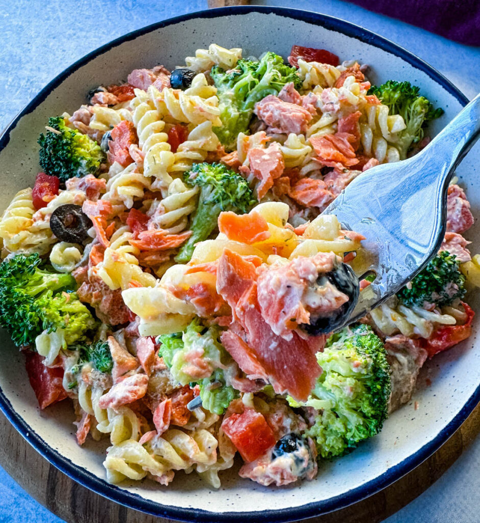 a forkful of salmon pasta salad with broccoli and tomatoes