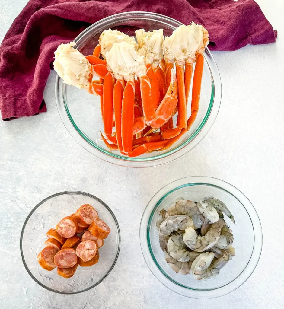 snow crab clusters, andouille sausage, and raw shrimp in separate glass bowls