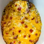 a wooden spoonful of hash brown casserole with cheese in a Crockpot slow cooker