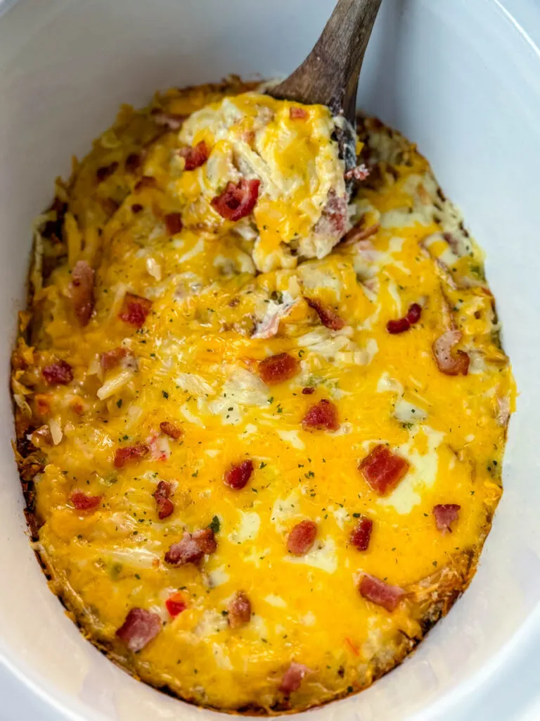 a wooden spoonful of hash brown casserole with cheese in a Crockpot slow cooker