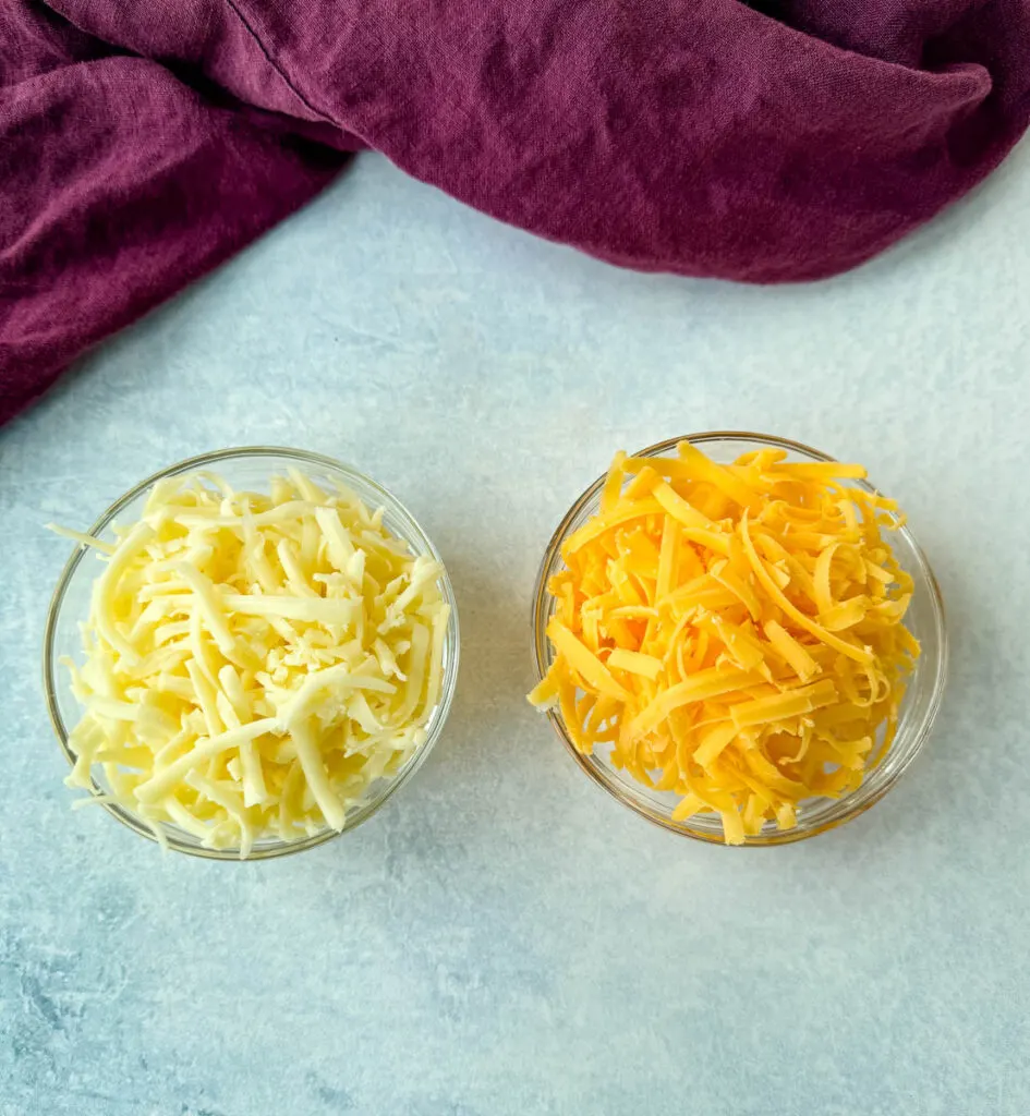 grated cheddar and mozzarella cheese in separate glass bowls