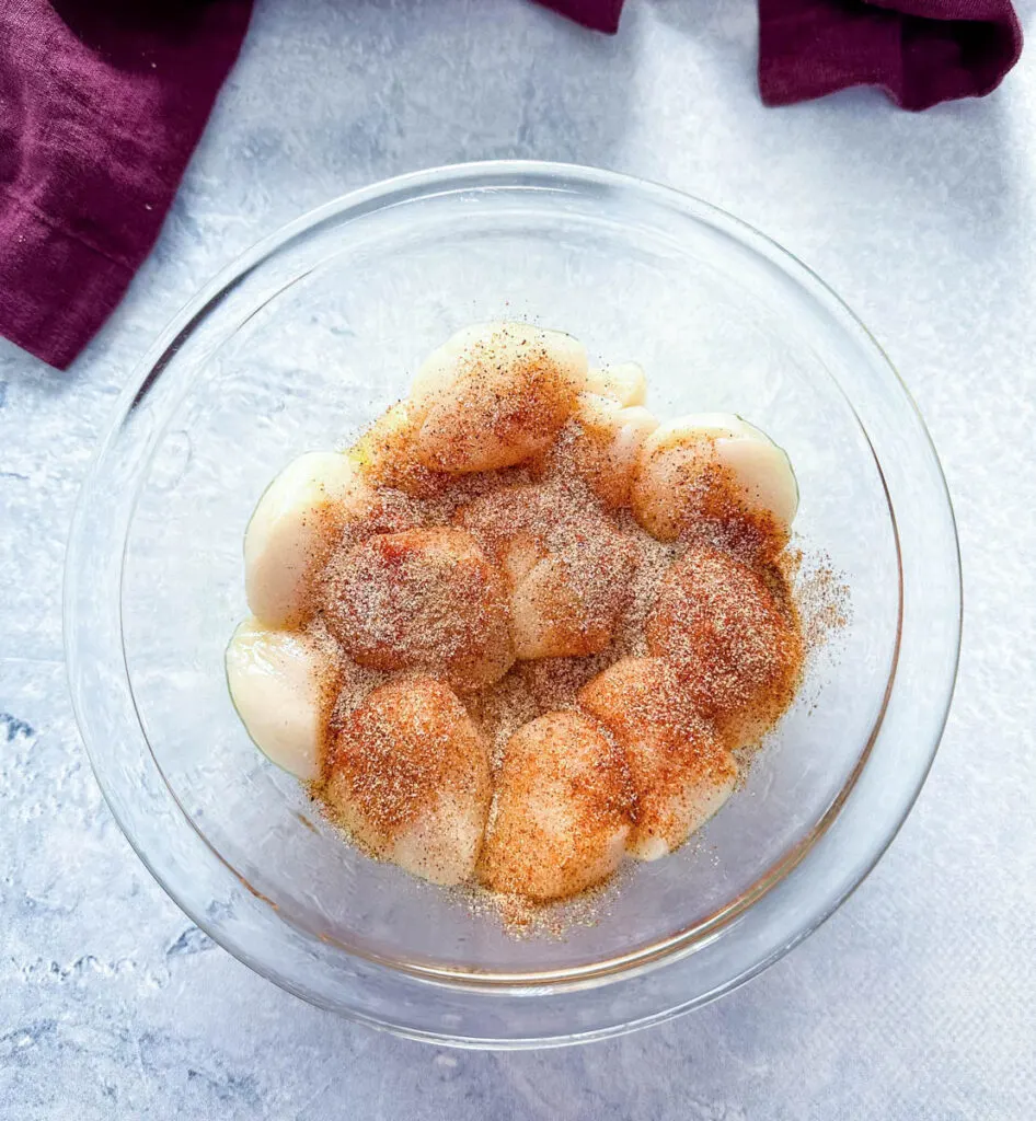 raw scallops seasoned with spices in a glass bowl