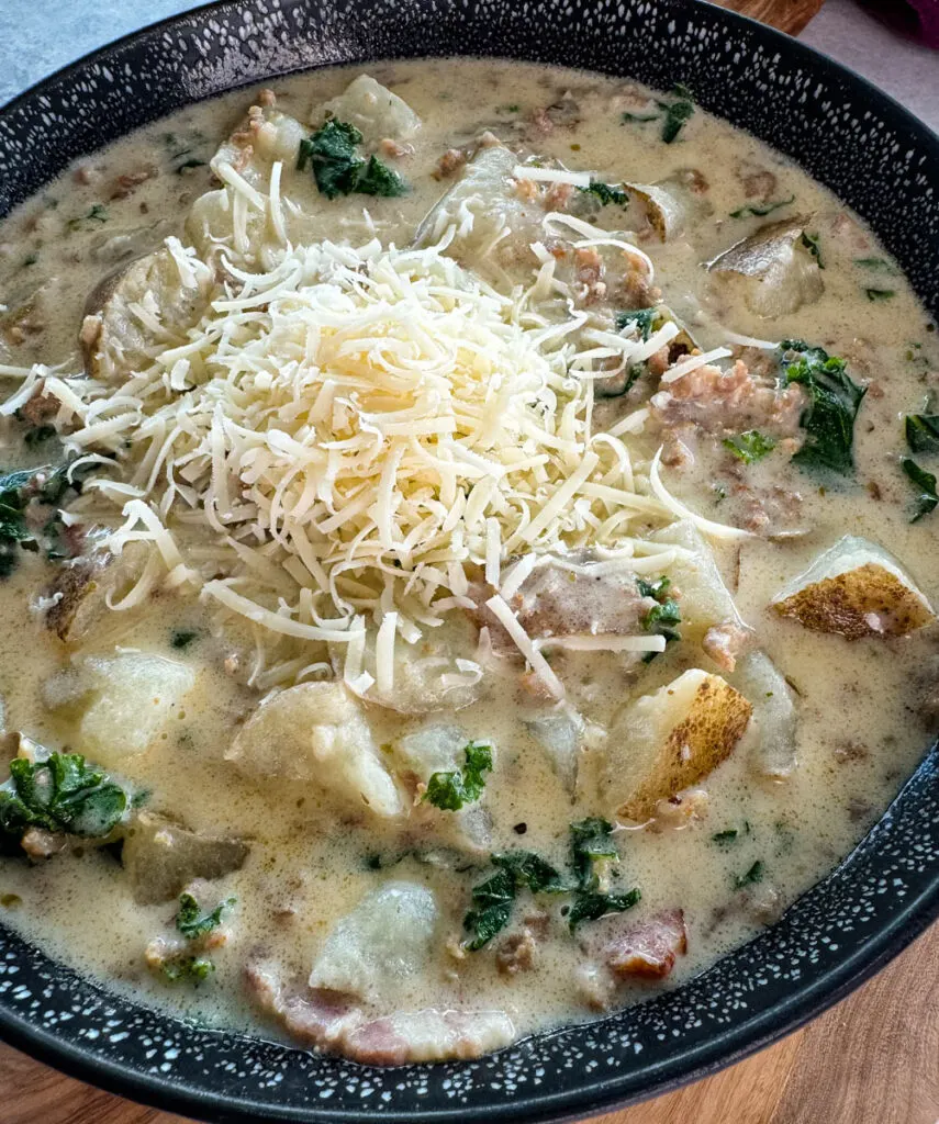 Italian sausage soup with potatoes and kale in a black bowl with grated parmesan cheese