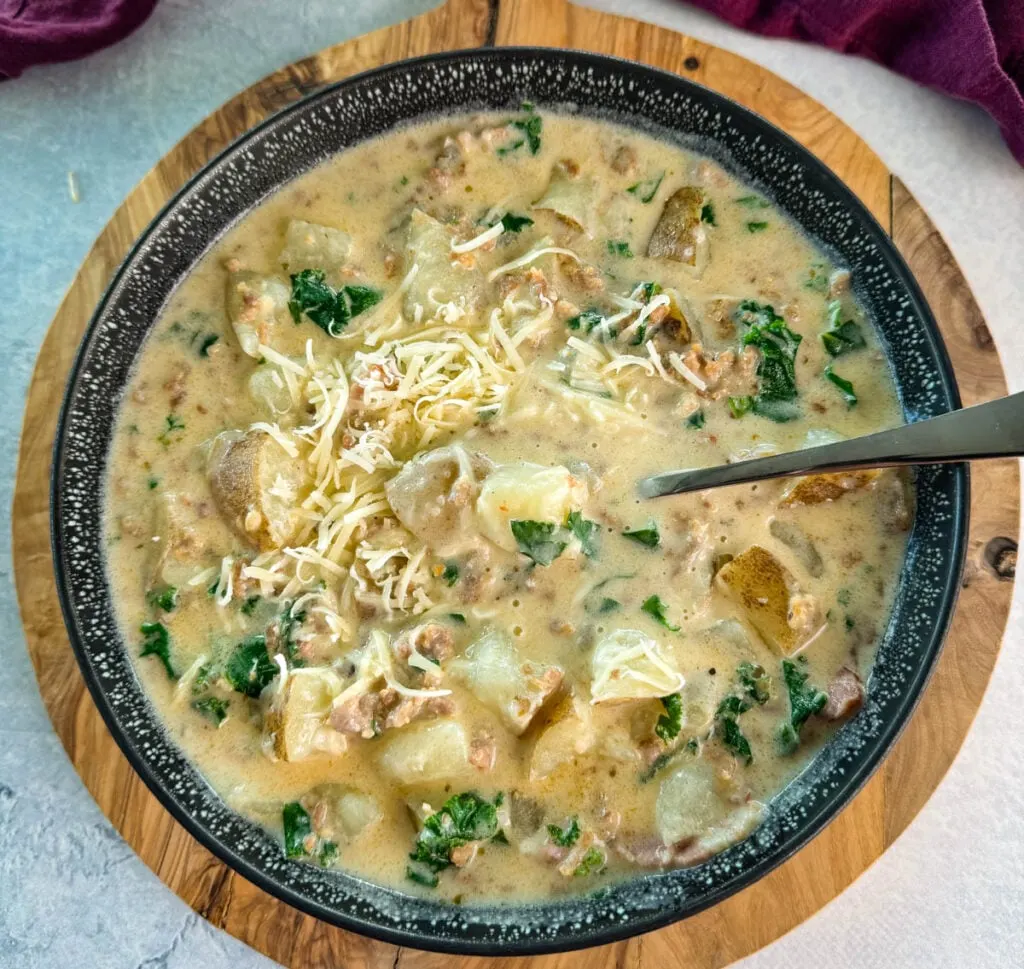 Italian sausage soup with potatoes and kale in a black bowl with grated parmesan cheese