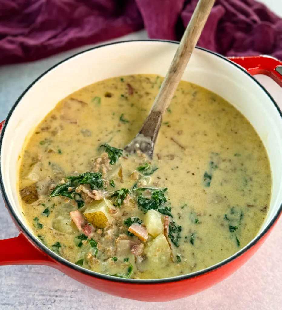 Italian sausage soup with potatoes and kale in a Dutch oven with a wooden spoon